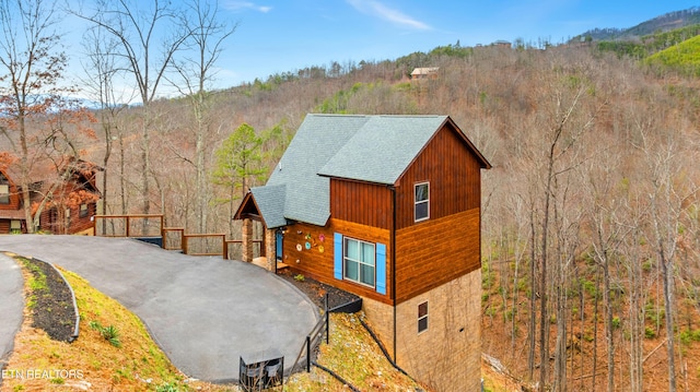 view of property exterior featuring stone siding, a shingled roof, and a forest view