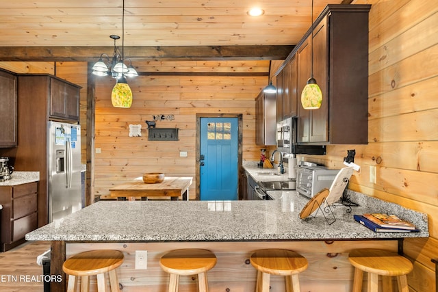 kitchen featuring wooden walls, a peninsula, light stone countertops, stainless steel appliances, and a sink