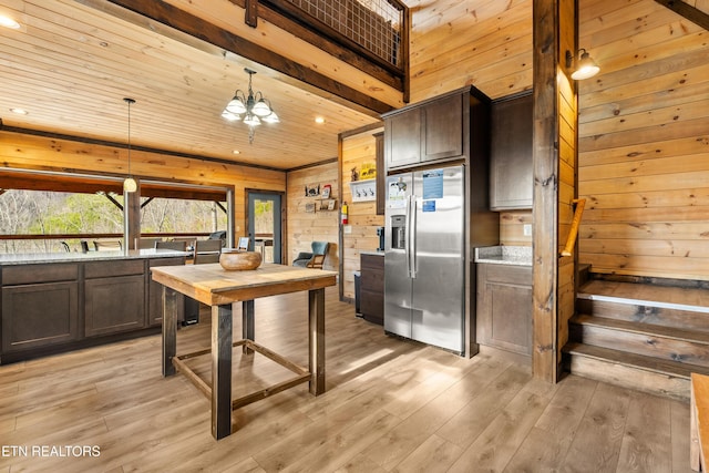 kitchen featuring stainless steel fridge, light wood-style flooring, decorative light fixtures, dark brown cabinets, and wood walls