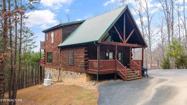 cabin featuring driveway, log siding, metal roof, covered porch, and central air condition unit