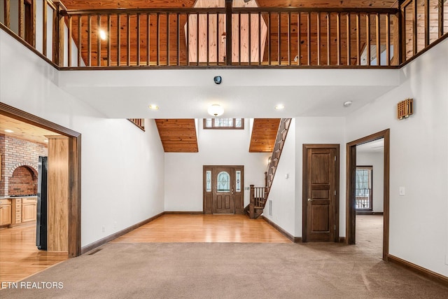 entryway featuring stairs, a high ceiling, baseboards, and light colored carpet