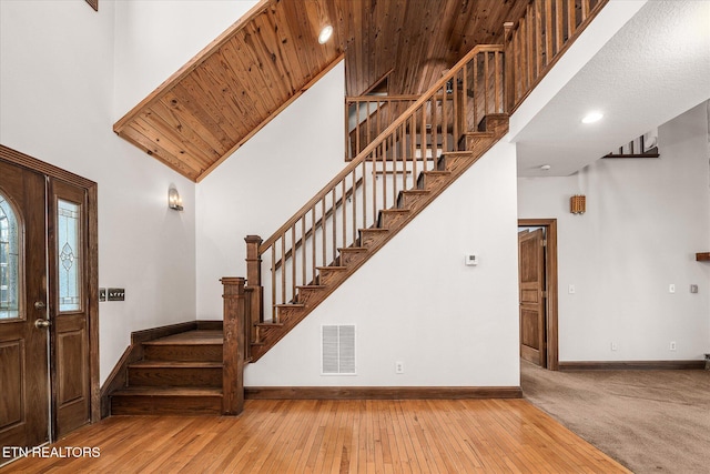 foyer with hardwood / wood-style floors, visible vents, a towering ceiling, and baseboards