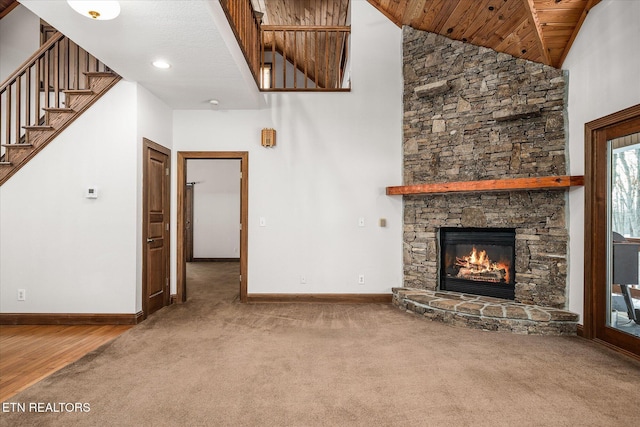 unfurnished living room featuring carpet floors, stairway, a stone fireplace, high vaulted ceiling, and baseboards