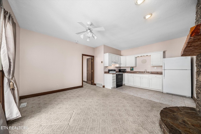 kitchen featuring black range with electric cooktop, light carpet, a sink, white cabinetry, and freestanding refrigerator