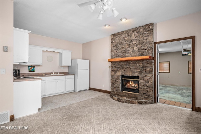 kitchen featuring light carpet, visible vents, freestanding refrigerator, white cabinetry, and a sink