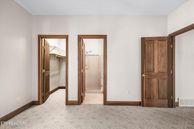 unfurnished bedroom featuring light carpet, a walk in closet, visible vents, and baseboards