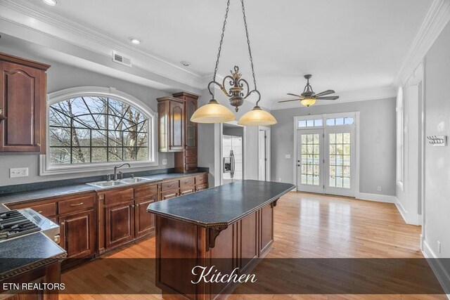 kitchen with dark countertops, visible vents, light wood-style flooring, a kitchen island, and a sink