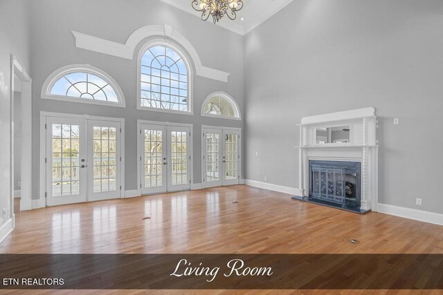 unfurnished living room with a fireplace with raised hearth, french doors, wood finished floors, and baseboards