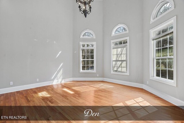 unfurnished dining area with a chandelier, a high ceiling, baseboards, and wood finished floors