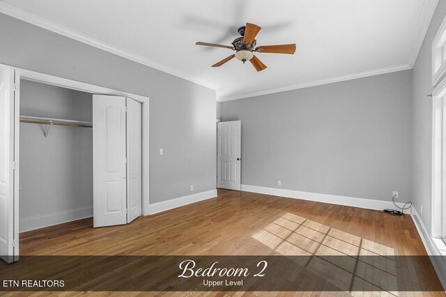 unfurnished bedroom with wood finished floors, a ceiling fan, baseboards, a closet, and crown molding