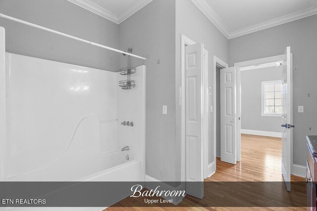 bathroom featuring crown molding, washtub / shower combination, baseboards, and wood finished floors