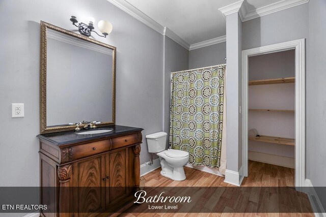 bathroom featuring toilet, wood finished floors, vanity, baseboards, and crown molding