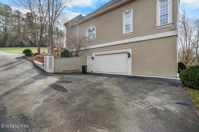 view of home's exterior with an attached garage, fence, aphalt driveway, and stucco siding