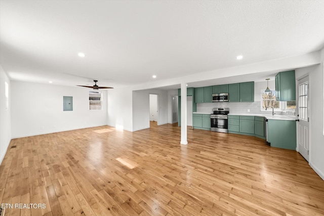 unfurnished living room featuring light wood finished floors, recessed lighting, a ceiling fan, a sink, and electric panel