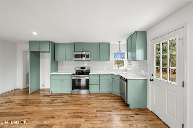 kitchen featuring appliances with stainless steel finishes, light countertops, a sink, and decorative light fixtures