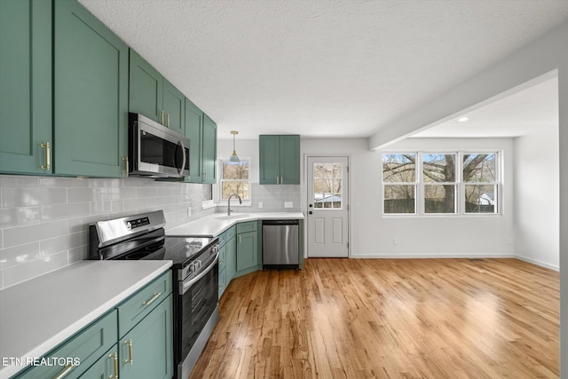 kitchen with appliances with stainless steel finishes, light countertops, a sink, and green cabinets