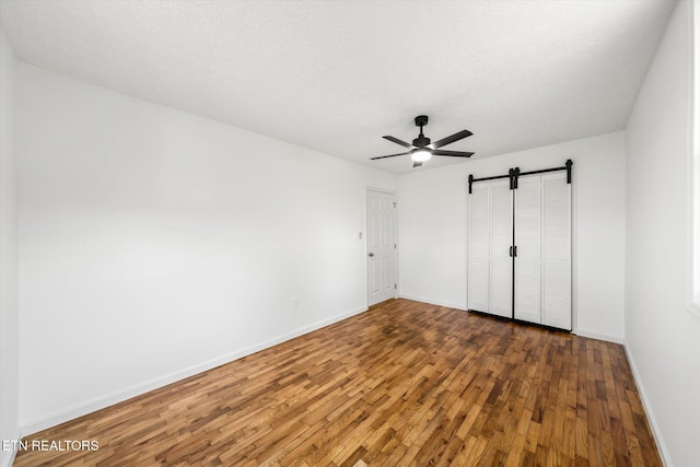 unfurnished bedroom featuring a textured ceiling, a barn door, a ceiling fan, baseboards, and dark wood finished floors