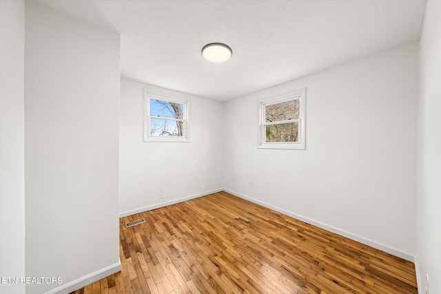 spare room with baseboards, plenty of natural light, visible vents, and wood finished floors