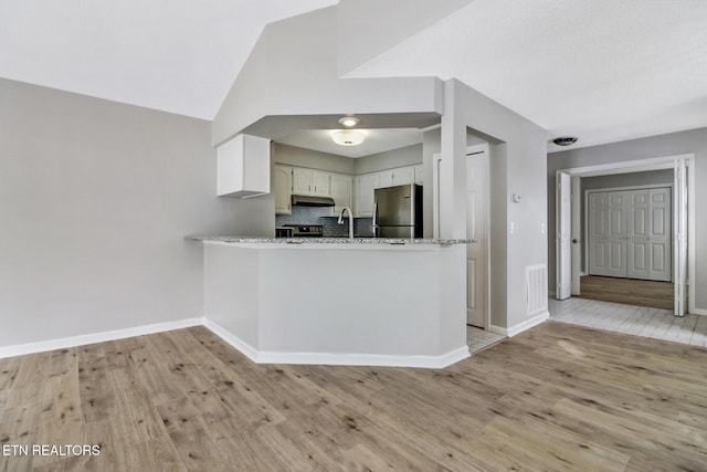 kitchen with freestanding refrigerator, white cabinetry, a peninsula, light stone countertops, and under cabinet range hood