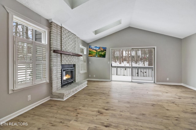 unfurnished living room featuring lofted ceiling, plenty of natural light, wood finished floors, and a brick fireplace