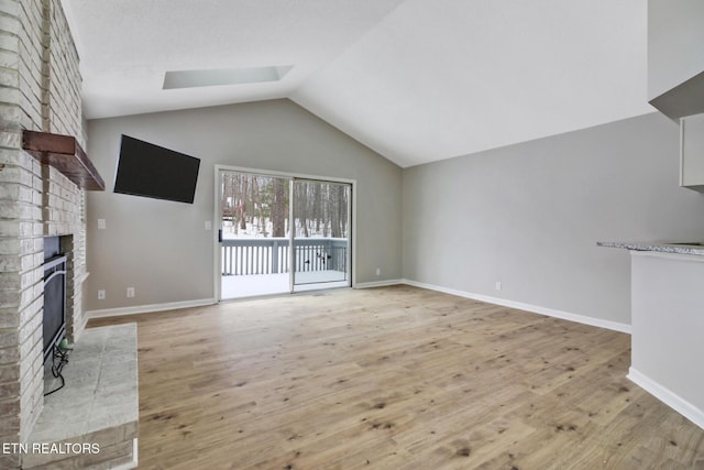 unfurnished living room with vaulted ceiling, light wood-type flooring, a brick fireplace, and baseboards