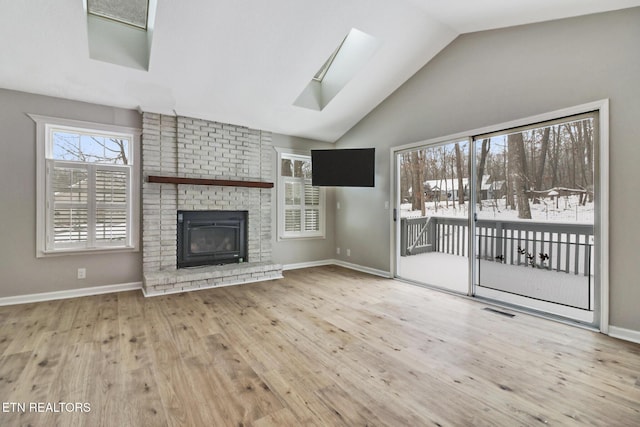 unfurnished living room featuring vaulted ceiling with skylight, visible vents, baseboards, light wood-style flooring, and a fireplace