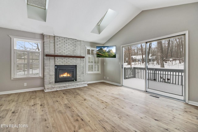 unfurnished living room with baseboards, visible vents, lofted ceiling with skylight, light wood-style floors, and a fireplace