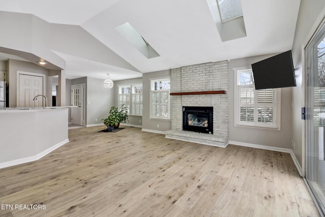 living area featuring light wood finished floors, lofted ceiling with skylight, a brick fireplace, and a wealth of natural light