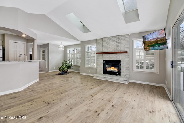 living area featuring a healthy amount of sunlight, light wood-style floors, vaulted ceiling with skylight, and a fireplace