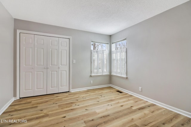 unfurnished bedroom featuring a textured ceiling, light wood-type flooring, visible vents, and baseboards