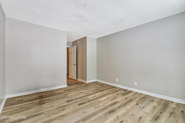 empty room featuring baseboards, a textured ceiling, and light wood finished floors