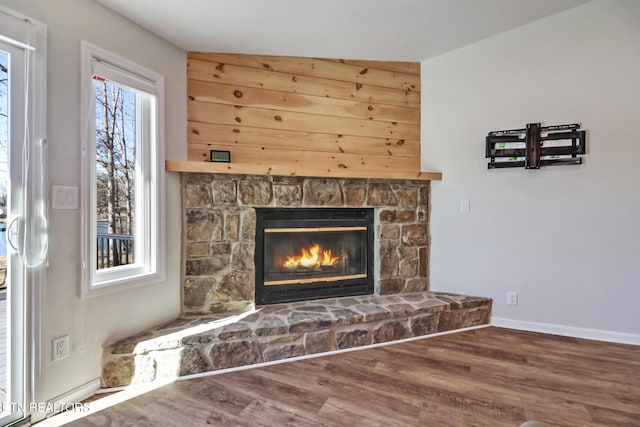 interior details featuring baseboards, a stone fireplace, and wood finished floors