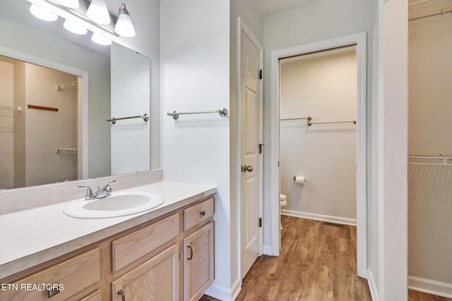 full bath featuring a walk in closet, toilet, wood finished floors, baseboards, and vanity