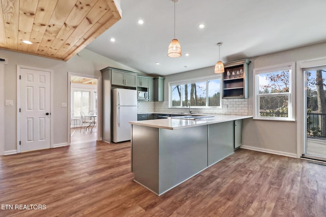kitchen featuring stainless steel microwave, backsplash, freestanding refrigerator, a peninsula, and dark wood-style flooring
