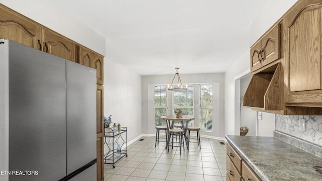 kitchen featuring hanging light fixtures, stainless steel refrigerator, light tile patterned flooring, tasteful backsplash, and a chandelier