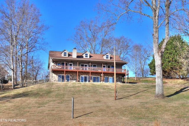 back of property with a chimney, stone siding, a yard, and a deck