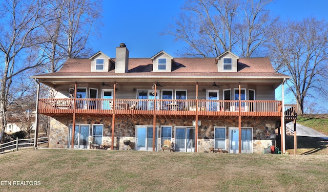 rear view of property with a yard, stone siding, fence, and a ceiling fan