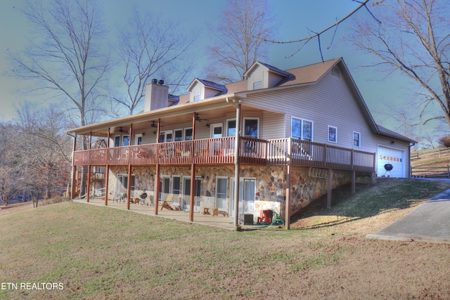 back of property featuring a garage, a ceiling fan, stone siding, a lawn, and a patio area