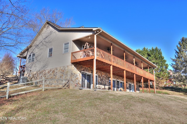 back of house with fence, a ceiling fan, a yard, stone siding, and a wooden deck