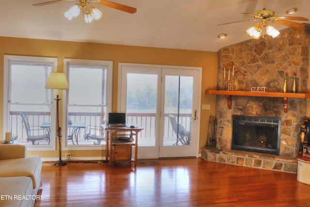 unfurnished living room with ceiling fan, plenty of natural light, a stone fireplace, and wood finished floors