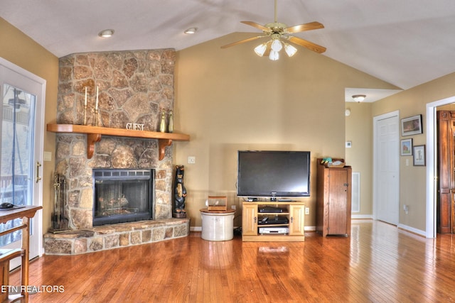 living area with baseboards, a ceiling fan, hardwood / wood-style floors, vaulted ceiling, and a stone fireplace