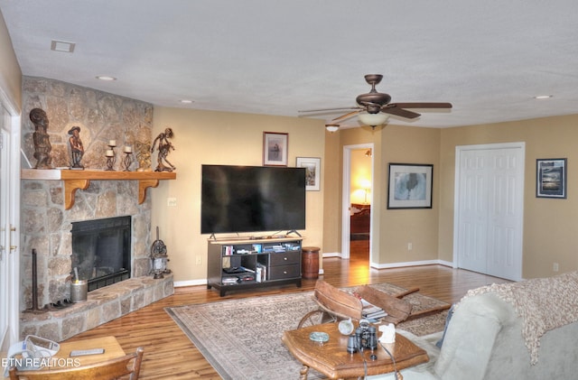 living area featuring ceiling fan, a stone fireplace, baseboards, and wood finished floors