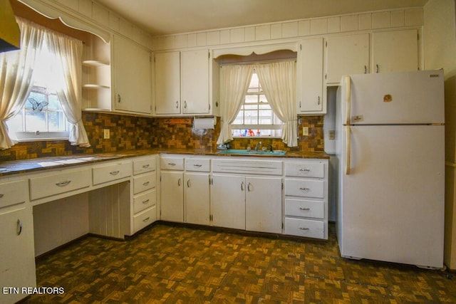 kitchen featuring a sink, white cabinets, freestanding refrigerator, open shelves, and tasteful backsplash