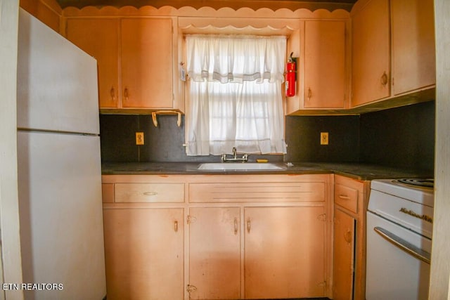 kitchen featuring tasteful backsplash, range, dark countertops, freestanding refrigerator, and a sink