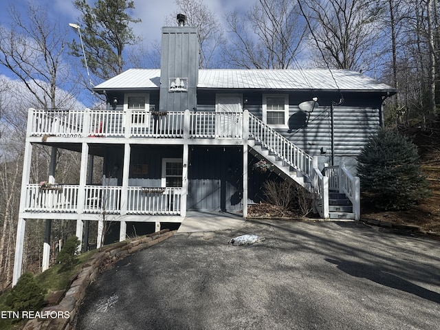 view of front of property featuring a deck, metal roof, a chimney, and stairs