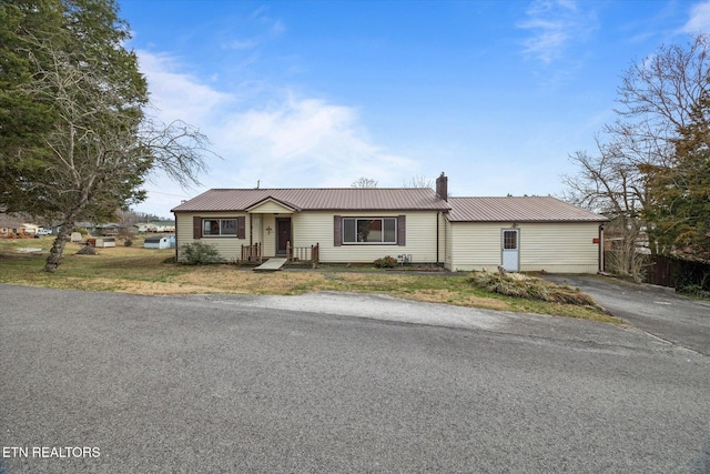 view of front of property with metal roof, a front yard, a chimney, and aphalt driveway