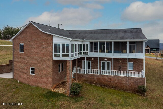 rear view of house with a sunroom, brick siding, and a yard