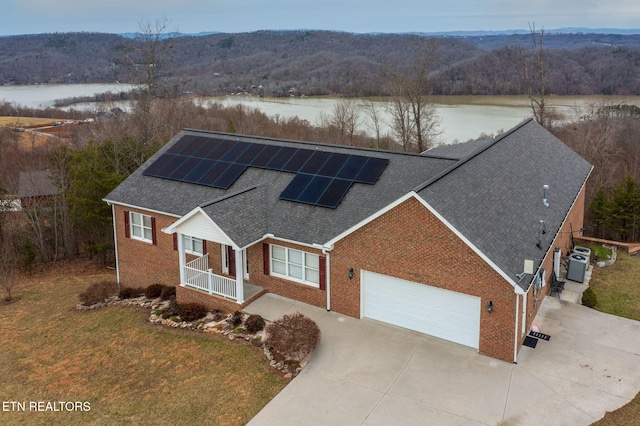 view of front of house featuring driveway, solar panels, roof with shingles, a water view, and a front lawn