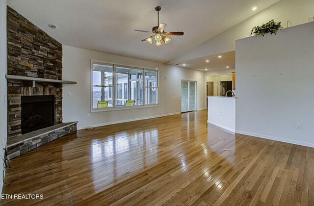 unfurnished living room with baseboards, a ceiling fan, a stone fireplace, light wood-type flooring, and high vaulted ceiling