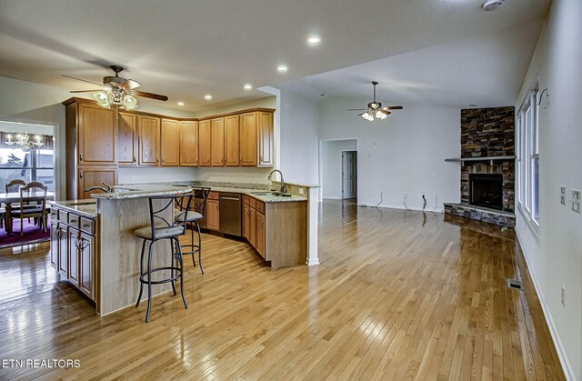 kitchen featuring brown cabinetry, open floor plan, a sink, a kitchen bar, and stainless steel dishwasher